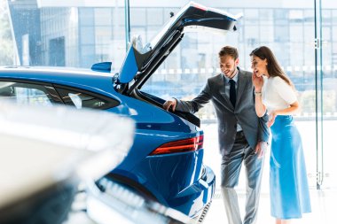 selective focus of bearded man and excited woman looking at car trunk  clipart