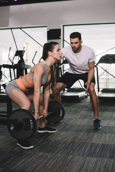 Yakışıklı sporcu kadın, genç sporcunun halter kaldırmasını öğretiyor.