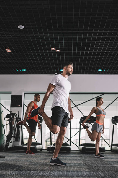 handsome trainer with multicultural athletes warming up in gym