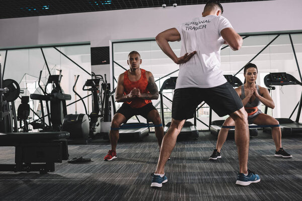 back view of personal trainer warming up in gym together with multicultural athletes
