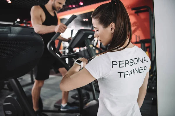 Joven Entrenador Mirando Rastreador Fitness Mientras Está Pie Deportista Corriendo — Foto de Stock