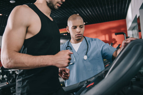 cropped view of sportsman on treadmill near attentive african american doctor