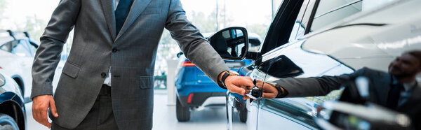 panoramic shot of man opening car door in car showroom 