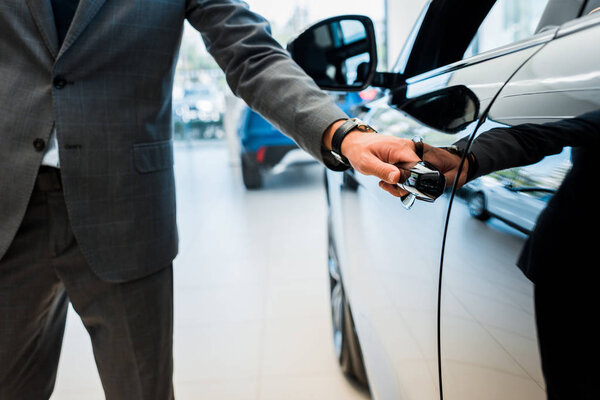 cropped view of man opening car door in car showroom 