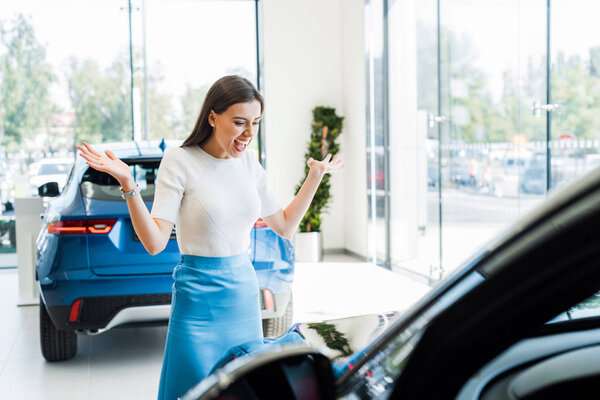 selective focus of excited woman gesturing while looking at black car 