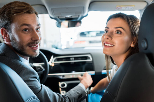 selective focus of happy bearded man sitting in car with attractive woman