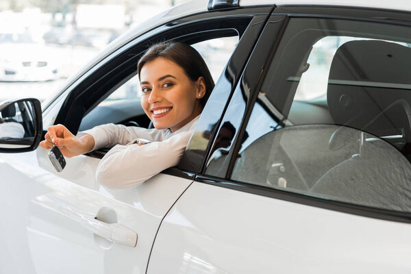 веселая молодая женщина держит ключ от машины, сидя в машине
 