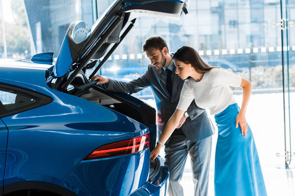 attractive woman standing near handsome bearded man and looking at car trunk 