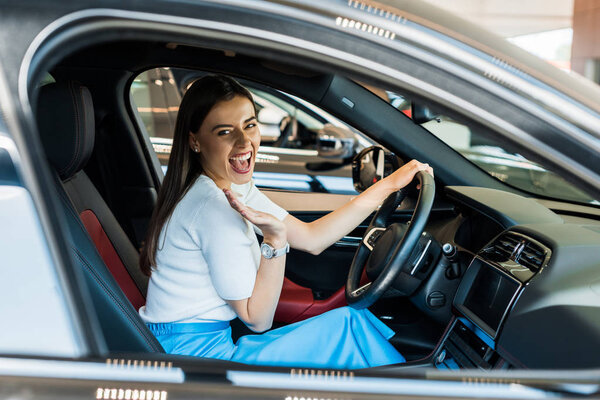 selective focus of excited woman waving hand while sitting in car 
