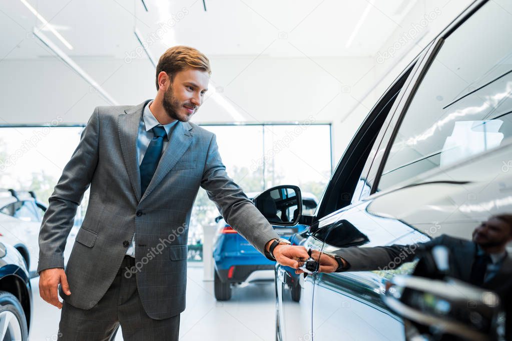 selective focus of bearded man opening car door in car showroom 