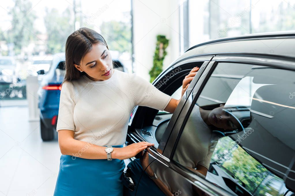 attractive woman looking at modern auto in car showroom 