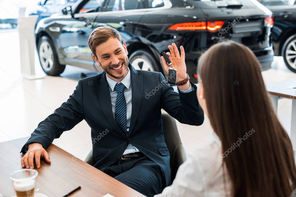 selective focus of happy bearded car dealer holding car keys near woman