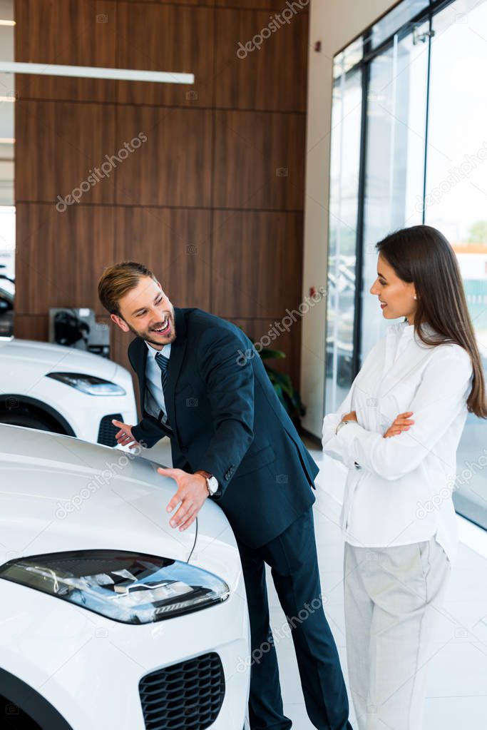 felice barbuto concessionario auto gesturing vicino donna con le braccia incrociate in auto showroom