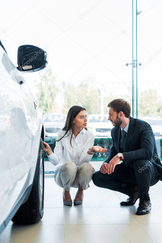 selective focus of woman sitting near car and gesturing while looking at bearded man 