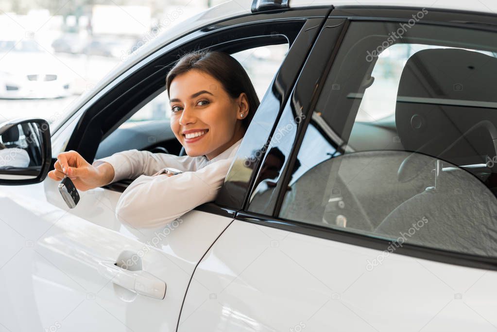 cheerful young woman holding car key while sitting in car 