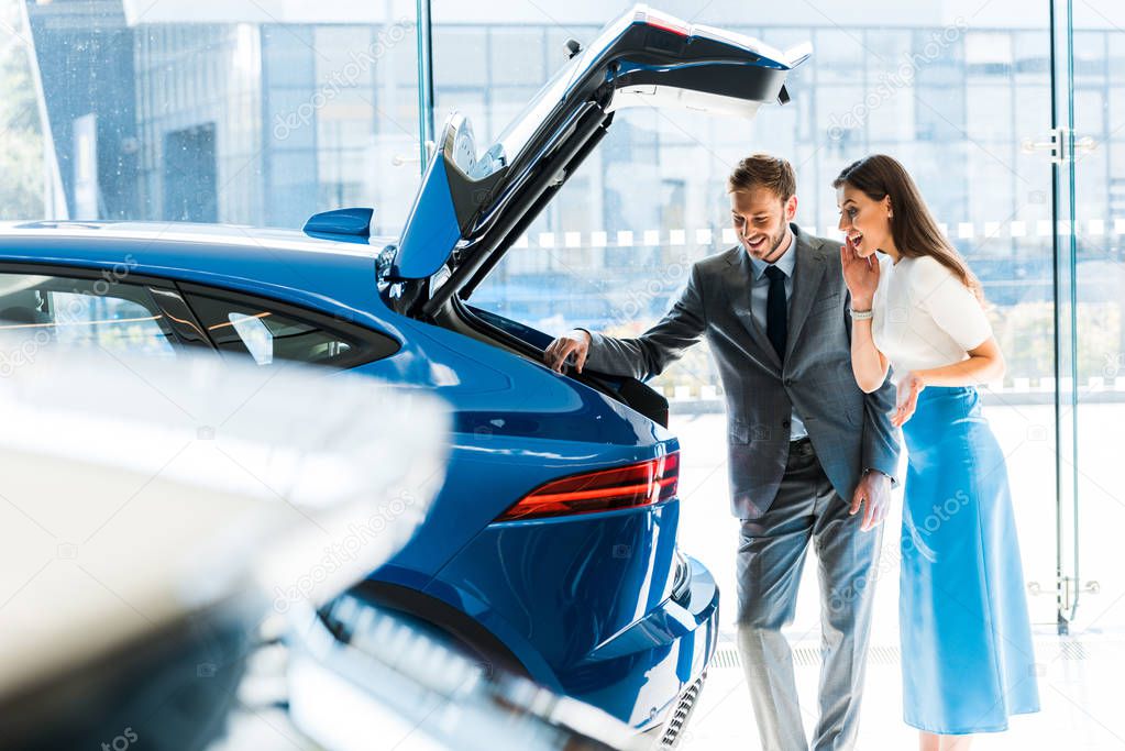 selective focus of bearded man and excited woman looking at car trunk 