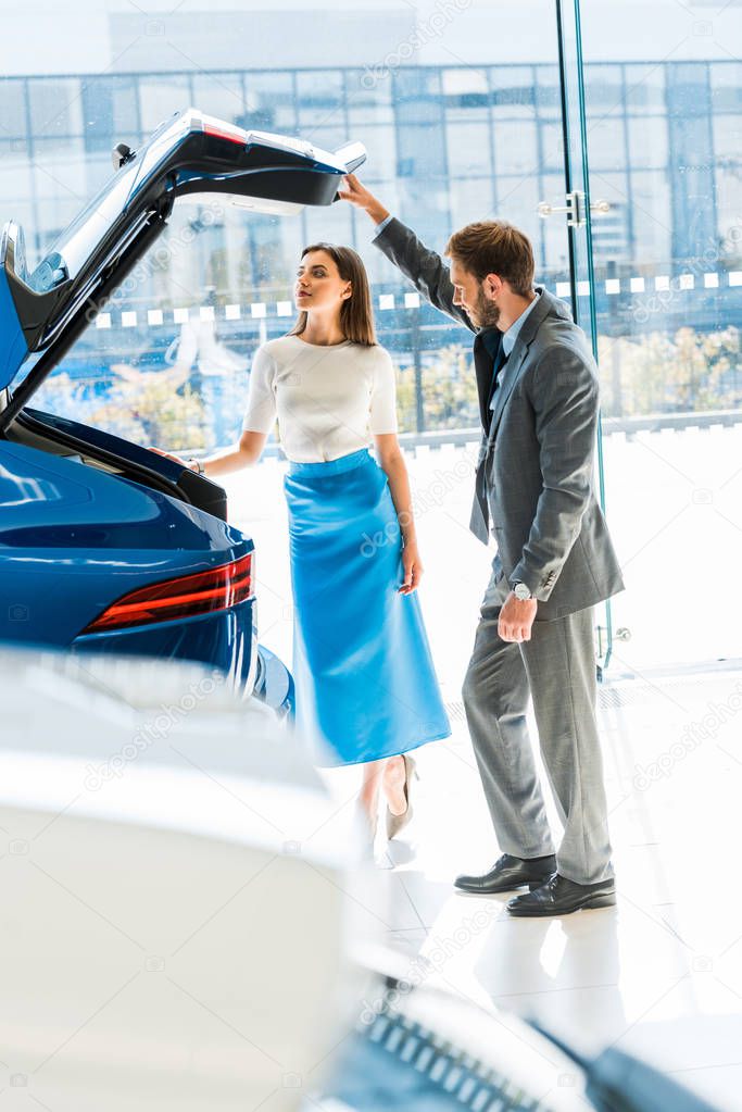 selective focus of beautiful woman and man standing near blue car 