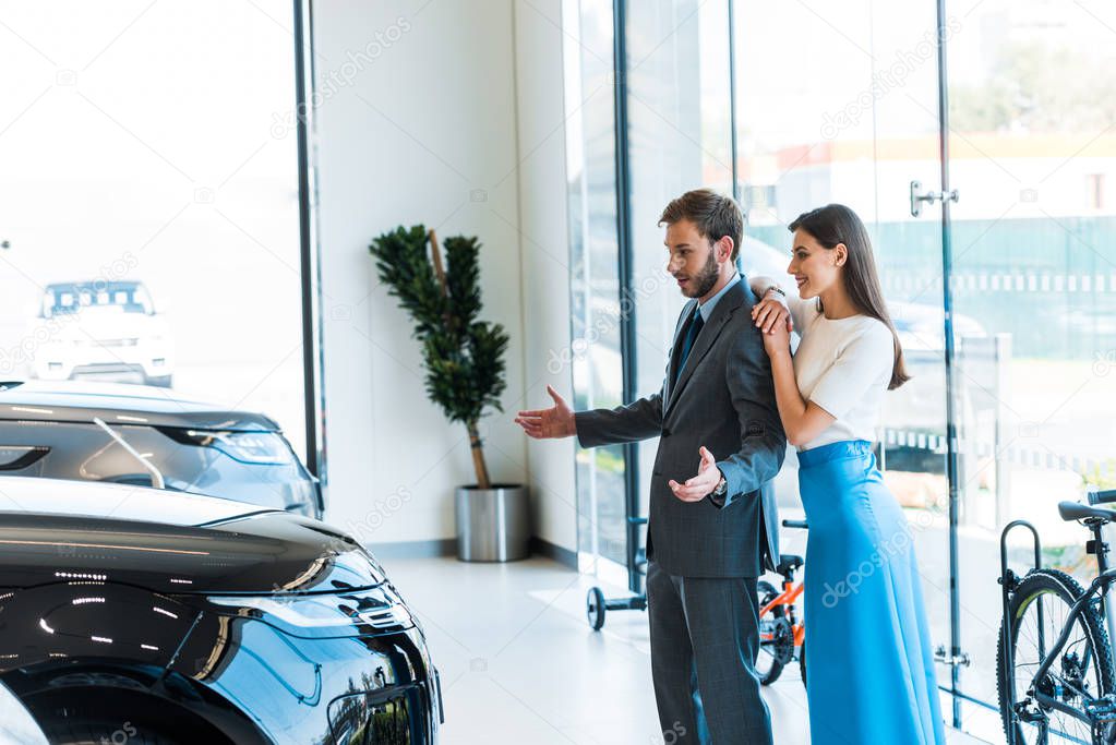 cheerful woman standing with handsome bearded man gesturing while looking at car 