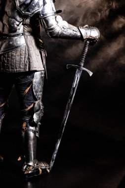 Zırhlı bir şövalyenin siyah arka planda kılıç tutuşu. 
