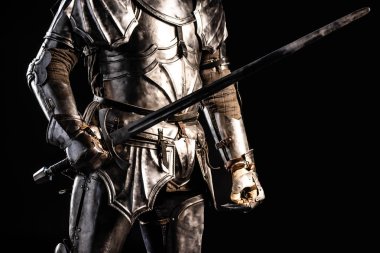 cropped view of knight in armor holding sword isolated on black  clipart