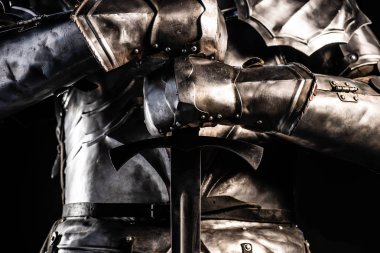 cropped view of knight in armor holding sword isolated on black  clipart