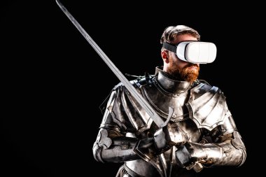 knight with virtual reality headset in armor holding sword isolated on black  clipart