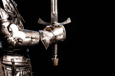 cropped view of knight in armor holding sword isolated on black  clipart