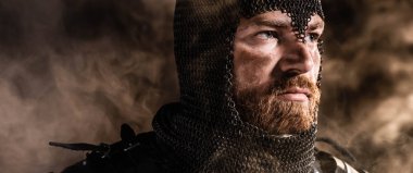 panoramic shot of handsome knight in armor looking away on black background clipart