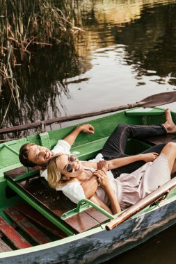 happy young couple relaxing in boat on lake and smiling at camera clipart