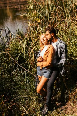 handsome young man embracing attractive girlfriend in thicket of sedge in park clipart