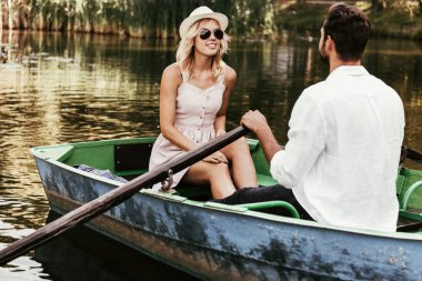 Sundress ve güneş gözlüklü gülümseyen kız kayıkçı sevgiliye bakıyor. 