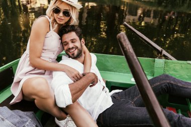 Çekici genç bir kadın teknede otururken mutlu erkek arkadaşına sarılıyor.