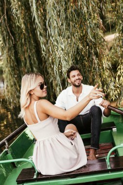 attractive young woman pointing with finger while sitting in boat near happy boyfriend clipart