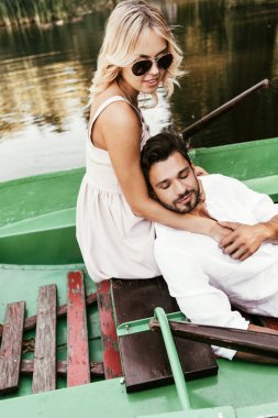 Gölde teknede otururken erkek arkadaşına sarılan güneş gözlüklü çekici bir kadın.