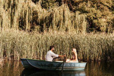 young couple in boat on river near thicket of sedge clipart