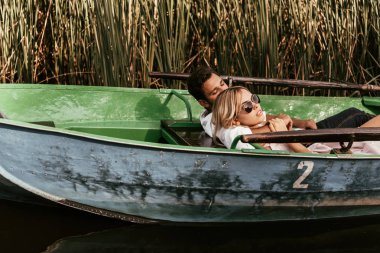 young couple relaxing in boat on river near thicket of sedge clipart