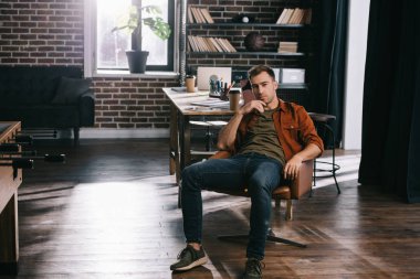 Genç, düşünceli iş adamı koltukta oturuyor ve kameraya bakıyor.