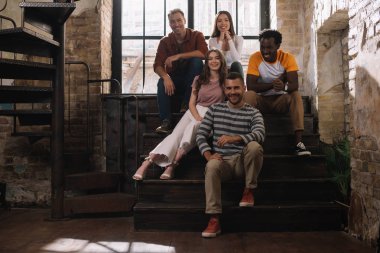 pozitif, genç çok kültürlü iş adamları merdivenlerde otururken kameraya gülümsüyorlar.