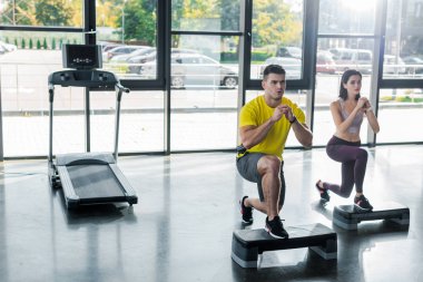 Yakışıklı sporcu ve sporcu kadın spor merkezinde adım platformlarında hamleler yapıyor.