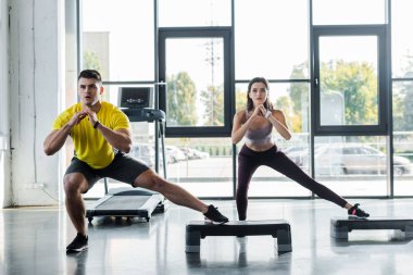 Yakışıklı sporcu ve sporcu kadın spor merkezinde adım platformlarında hamleler yapıyor.
