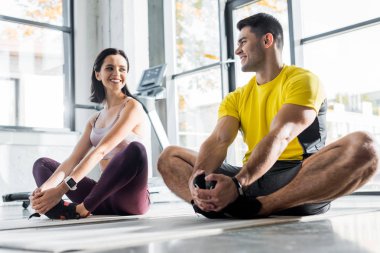 Gülümseyen sporcu ve sporcu kadın spor merkezinde spor paspasları üzerinde geriniyorlar.