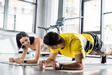 Sporcu ve gülümseyen sporcu kadın spor merkezindeki spor paspasları üzerinde tahta yapıyor.