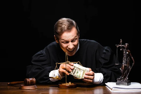 Mosolygó Bíró Bírósági Köntösben Asztalnál Kezében Dollár Bankjegyek Elszigetelt Fekete — Stock Fotó