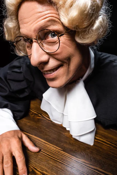 Sorrindo Juiz Roupão Judicial Peruca Sentado Mesa Isolado Preto — Fotografia de Stock