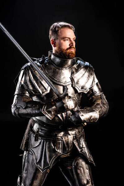 Красивый рыцарь в доспехах держит меч изолированный на черном
