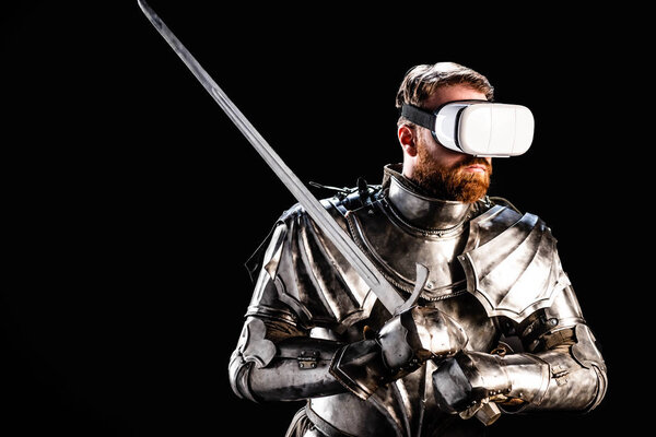 Рыцарь с гарнитурой виртуальной реальности в броне, держащий меч изолированный на черном
 