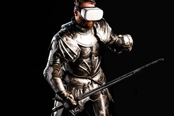 Рыцарь с гарнитурой виртуальной реальности в доспехах, держа меч и сражаясь изолированно на черном
 