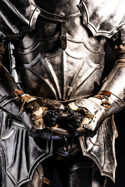 КИЕВ, УКРАИНА - 9 ОКТЯБРЯ 2019: обрезанный вид рыцаря в броне, держащего джойстик изолированным на черном
 