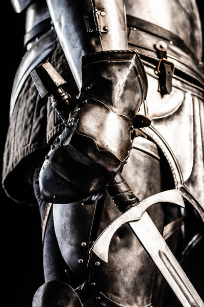Cropped view of knight in armor holding sword isolated on black