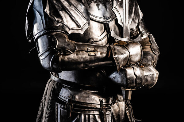 обрезанный вид рыцаря в доспехах, держащего меч изолированный на черном
 